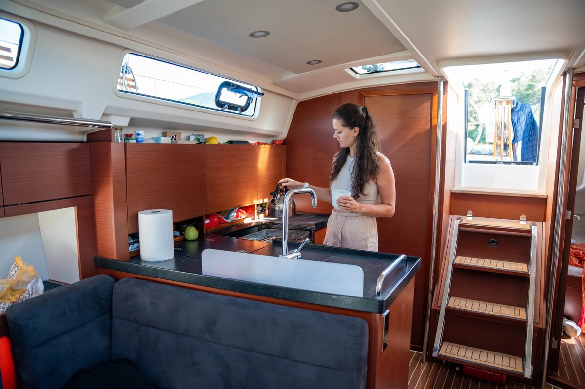 Young woman standing and preparing tea in kitchen in cabin of modern yacht during sailing in sea