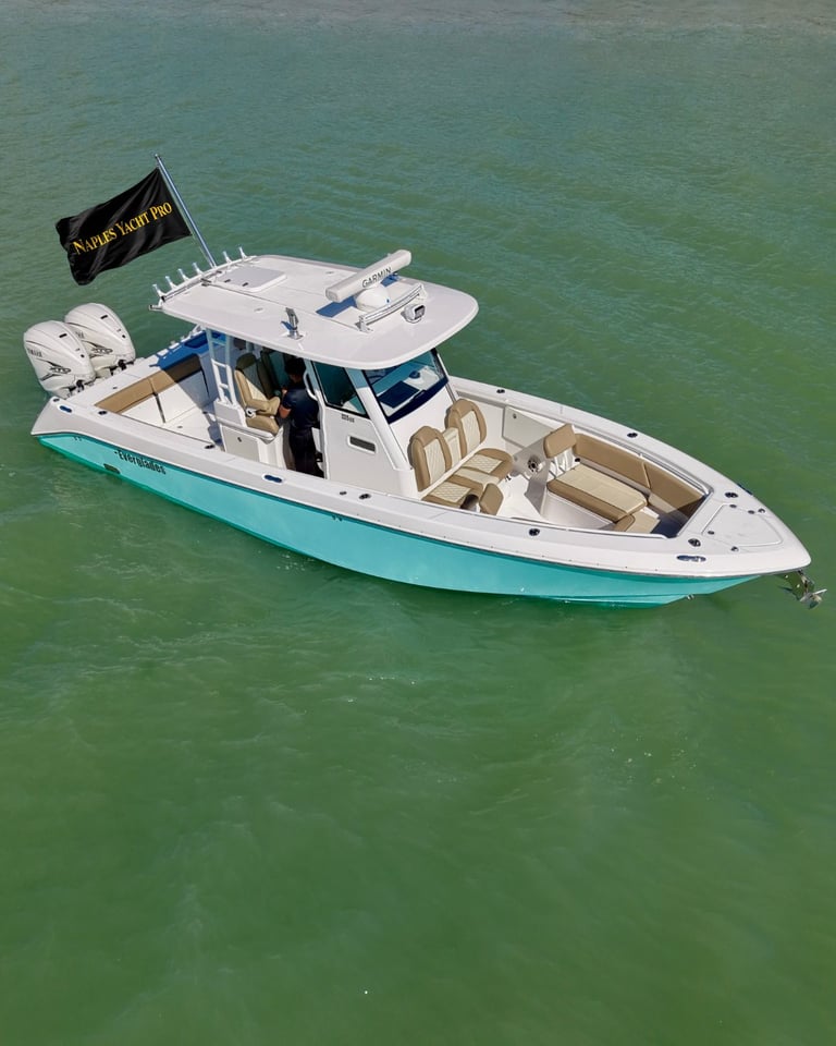 White and turquoise fishing boat with cabin anchored in shallow green water, viewed from above