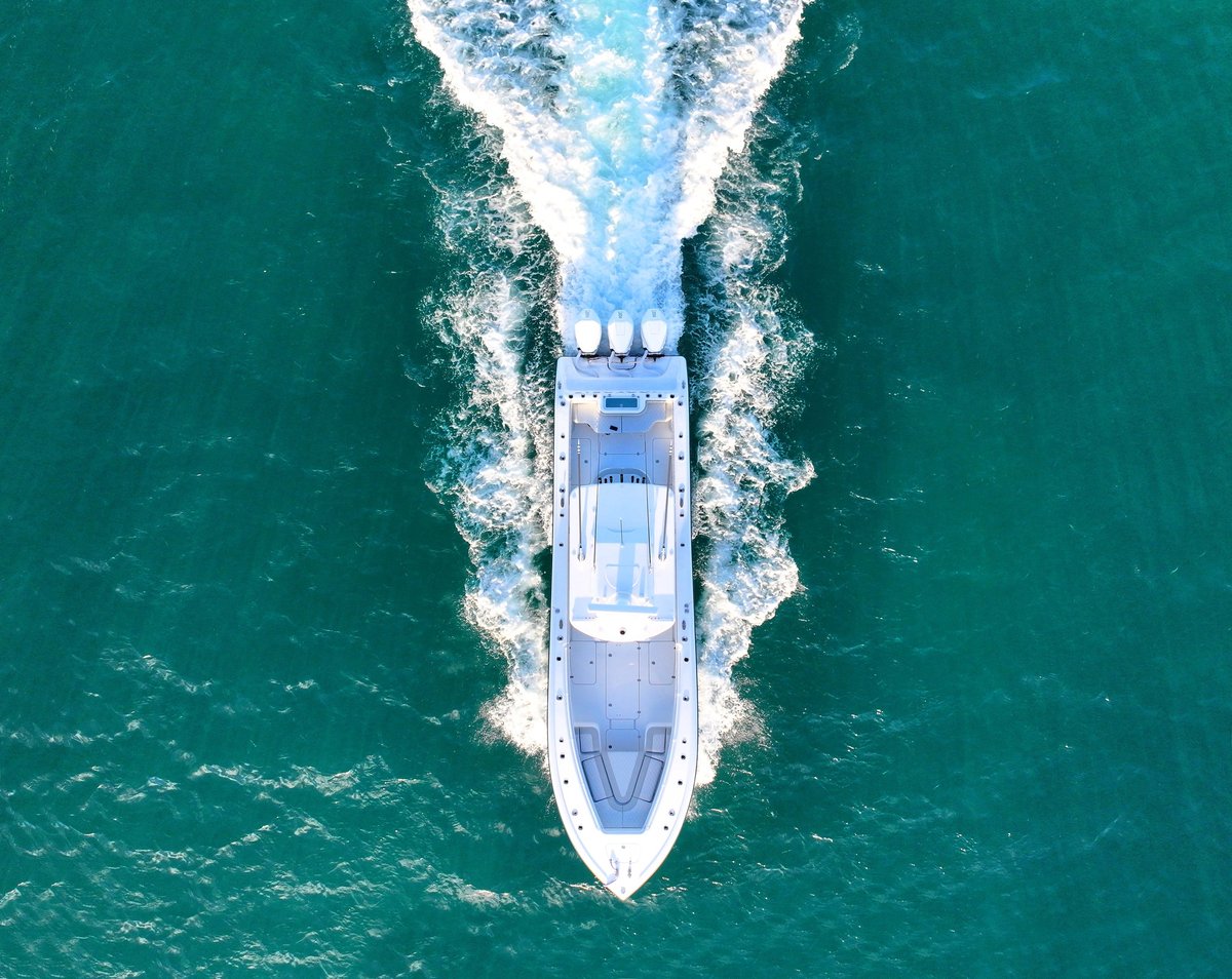 Aerial view of a cruise ship moving through turquoise ocean water with white wake trail